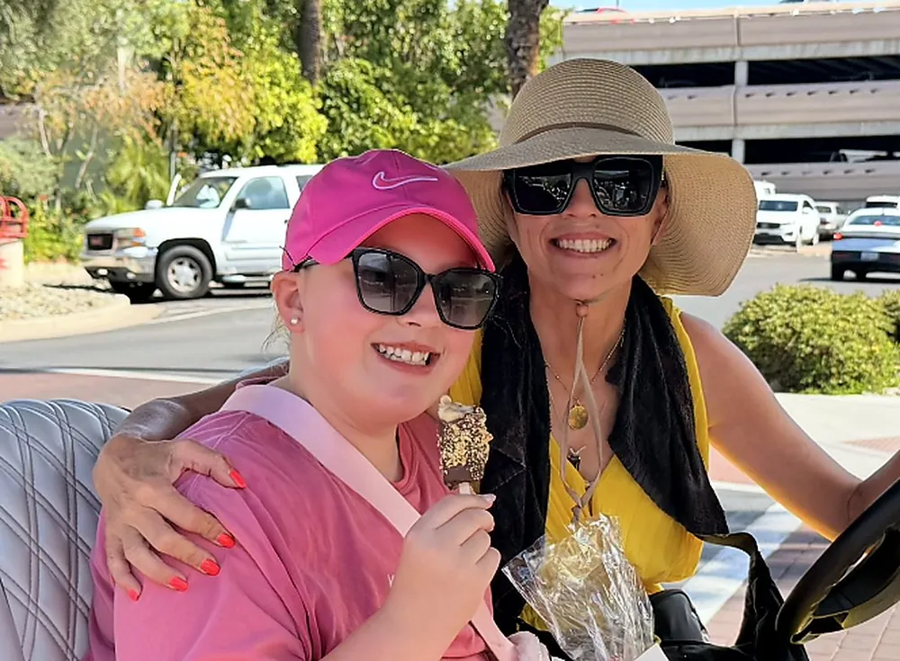 A mom and her daughter on a golf cart, the daughter holding a chocolate dipped banana