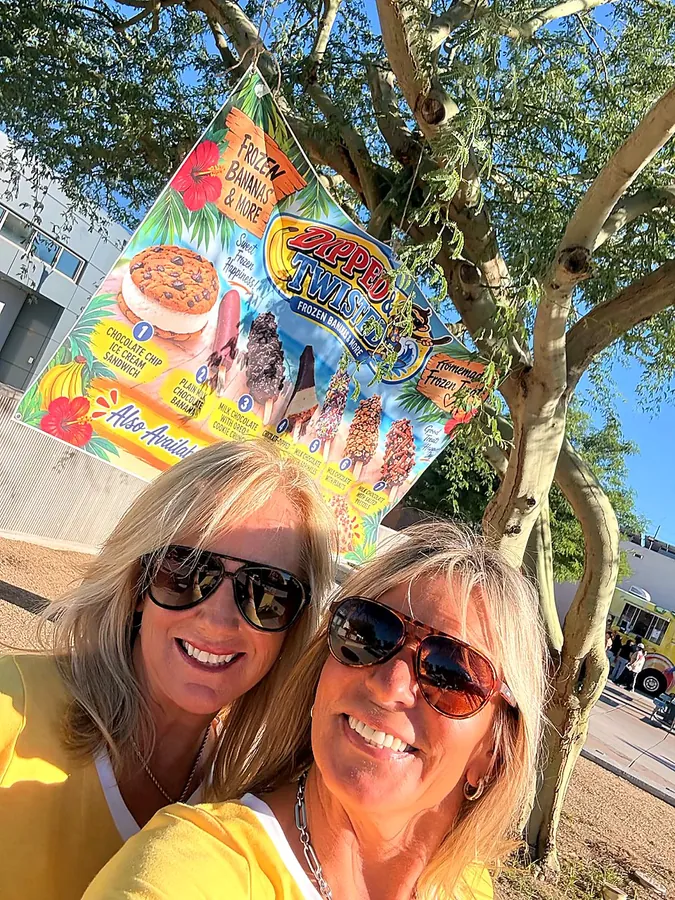 Jules and Elena smiling in front of a Dipped and Twisted menu banner