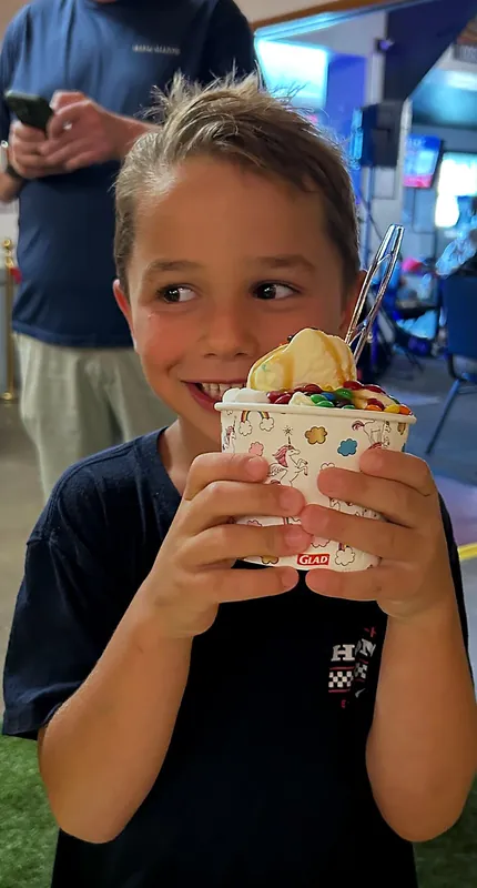 A smiling boy holding up a cup of ice cream with toppings